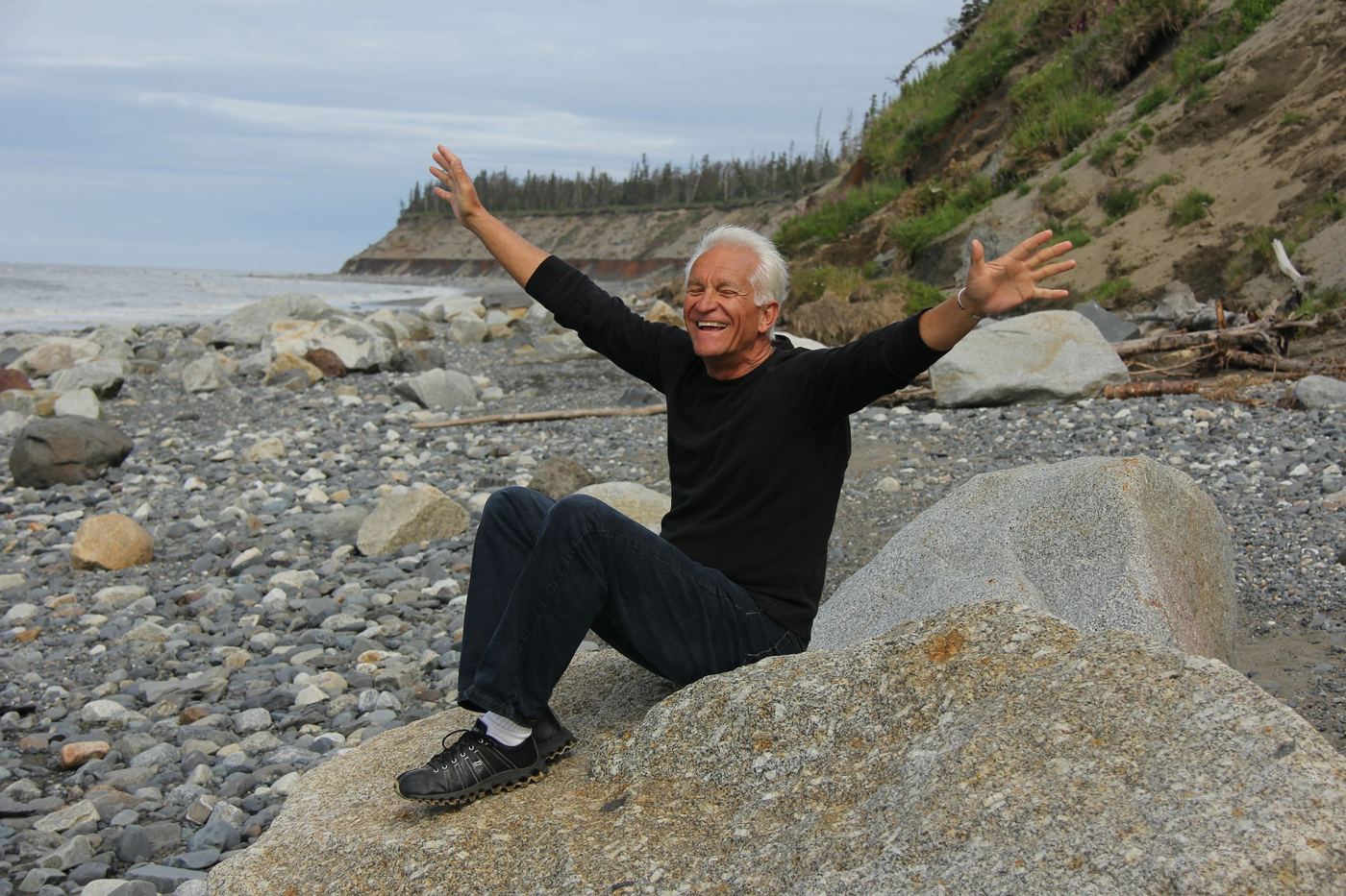 A joyful older man with arms raised on a rocky beach