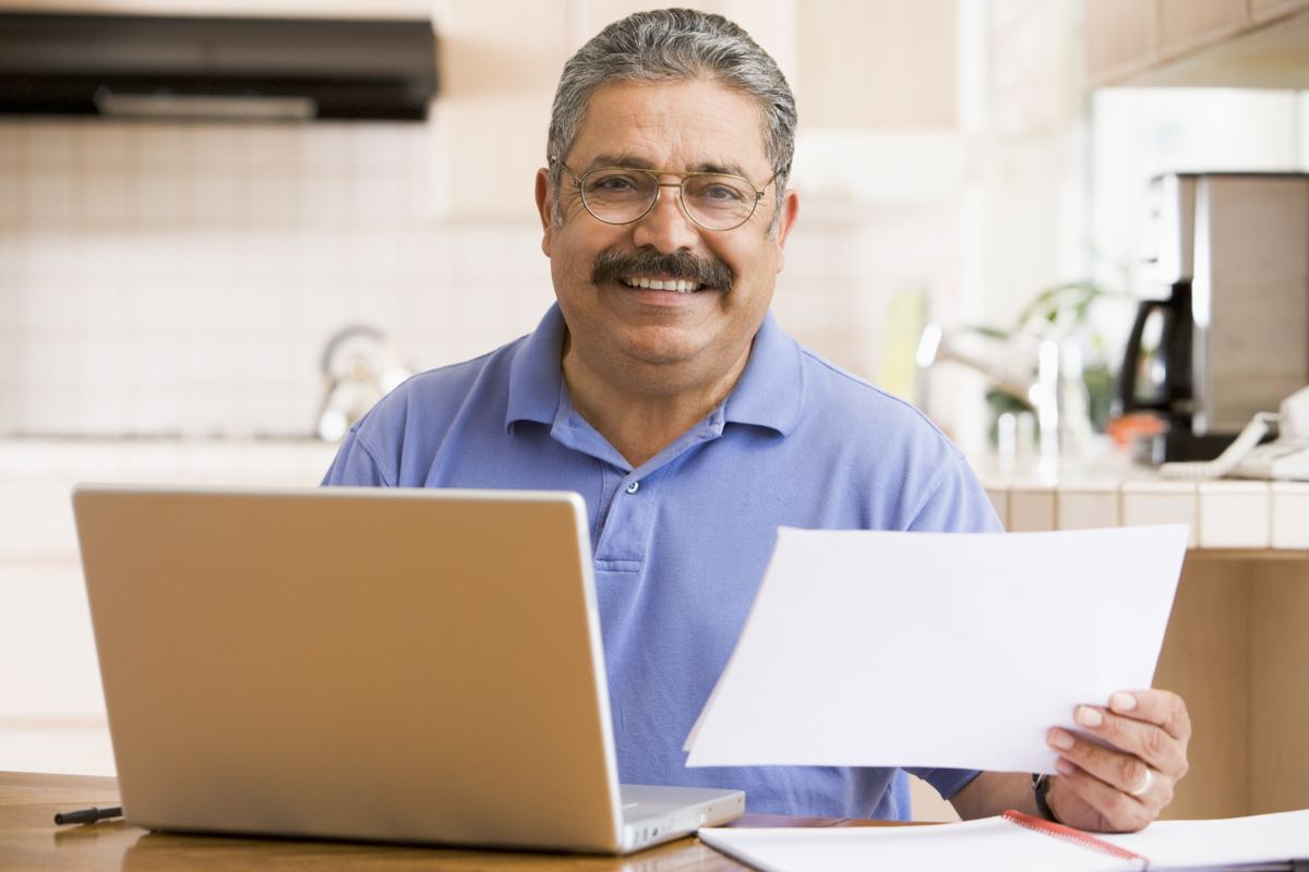 A smiling man reviews paperwork at his laptop