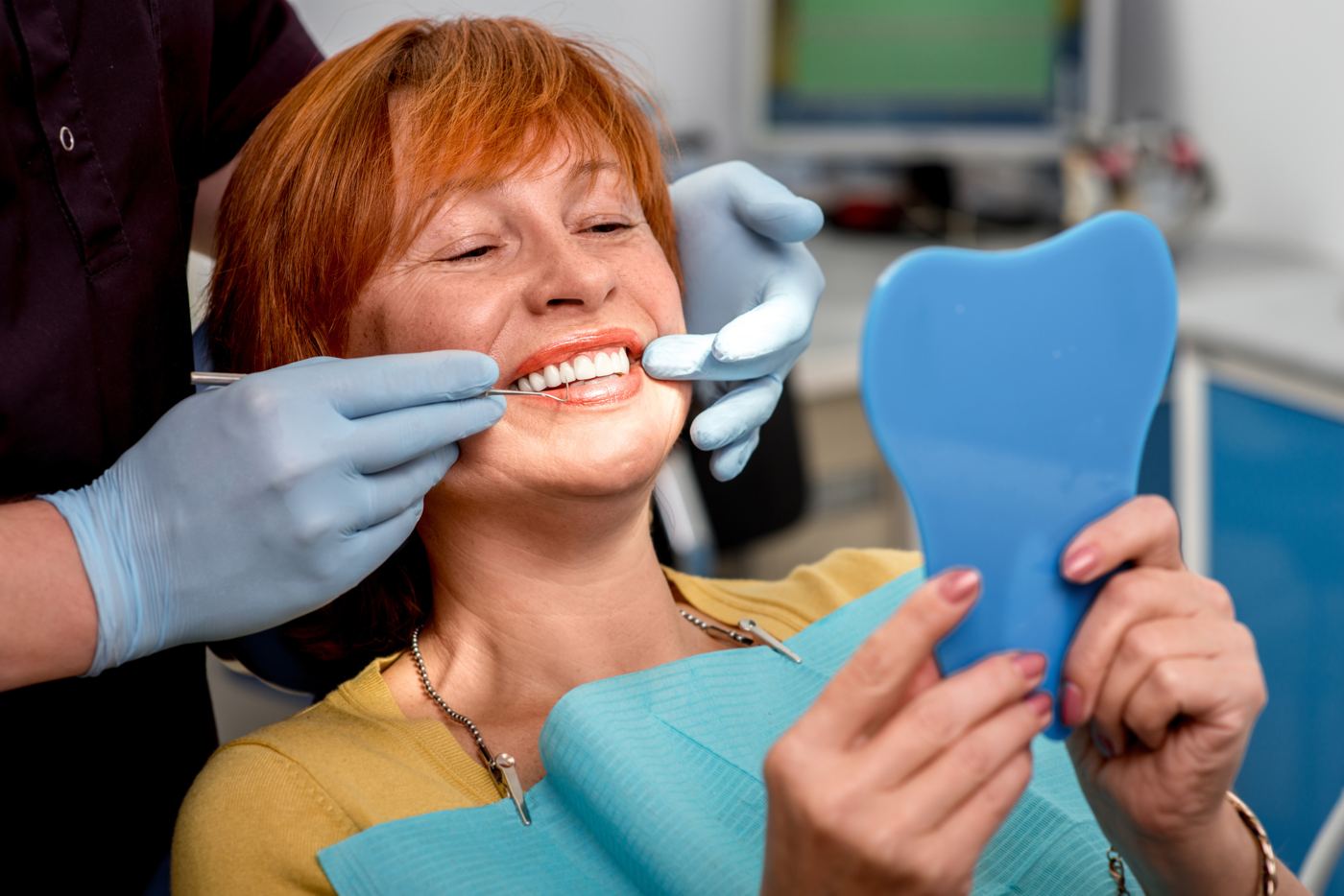 A smiling patient checks her new smile in a mirror at the dentist